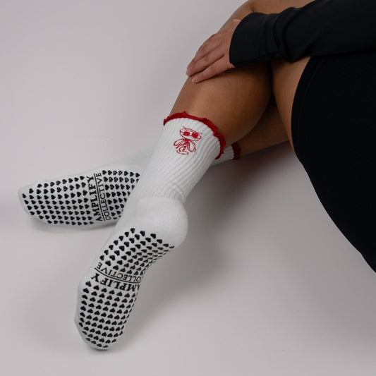 Person wearing white socks with black textured sole and red accents on a plain background