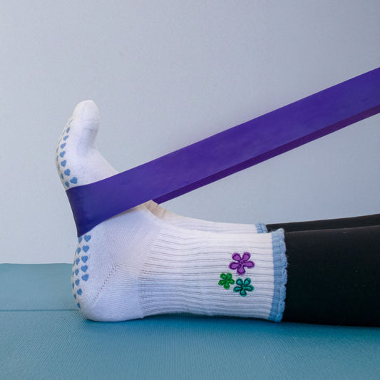 White sock with blue accents and a clover design, worn on a foot, with a purple resistance band.